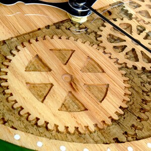 May include: Close-up of a wooden clock face with intricate gear designs. The gears are carved into the wood and have a natural brown color.