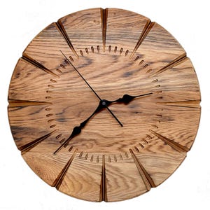 May include: A round wall clock crafted from natural wood with a prominent grain pattern. The face features twelve deep, radiating grooves extending from the center to the edge, with small carved indentations marking the minutes and black hands.