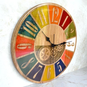 May include: A colorful round clock with Roman numeral hour markers and a gear design in the center. The clock face is made of wood and has a colorful, segmented design with each segment featuring a different color.