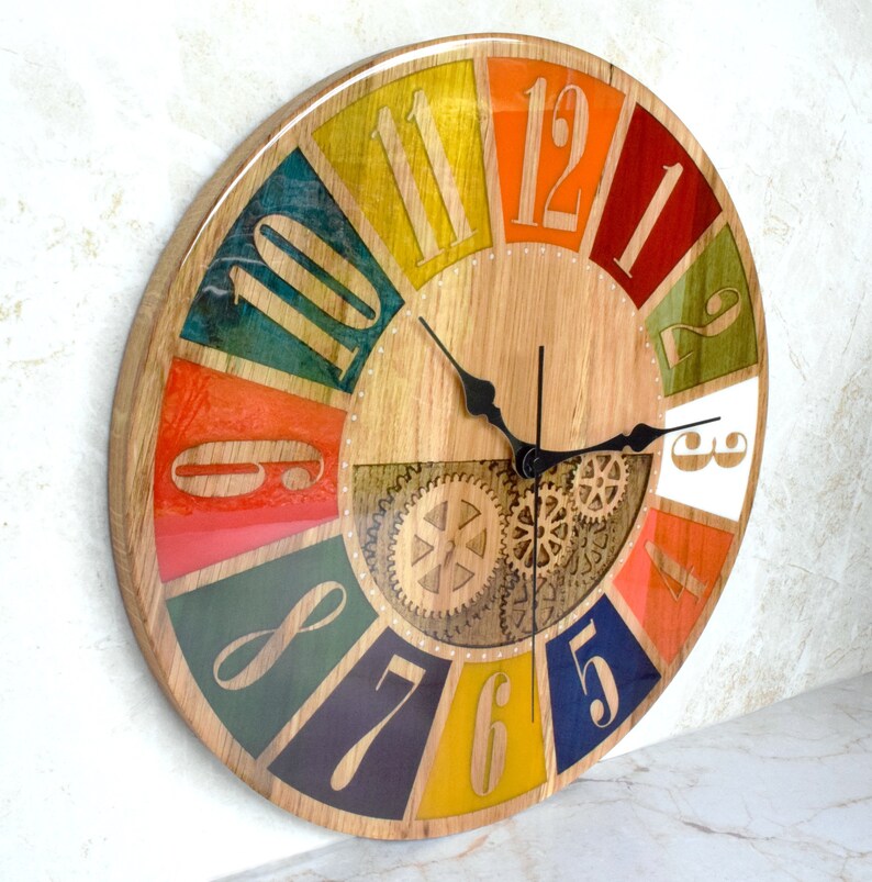 May include: A colorful round clock with Roman numeral hour markers and a gear design in the center. The clock face is made of wood and has a colorful, segmented design with each segment featuring a different color.