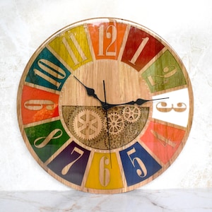 May include: A colorful wooden clock with Roman numeral hour markers and a gear design. The clock face is divided into 12 sections, each painted a different color, including red, orange, yellow, green, blue, and purple. The clock hands are black.