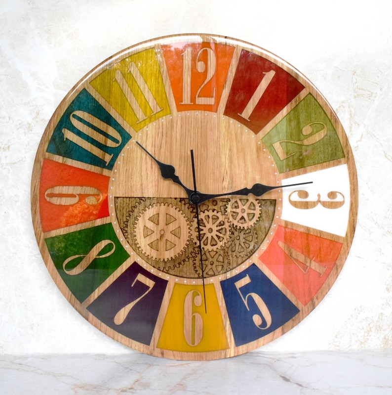 May include: A colorful wooden clock with Roman numeral hour markers and a gear design. The clock face is divided into 12 sections, each painted a different color, including red, orange, yellow, green, blue, and purple. The clock hands are black.