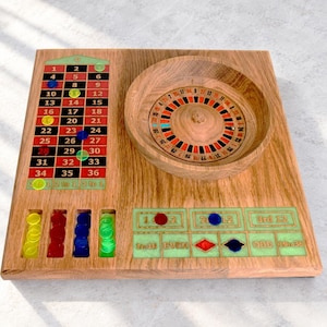 May include: A wooden roulette game board featuring a circular spinning wheel, a numbered betting grid with red and black squares, and integrated slots for colored plastic chips. The board includes text labels for betting options like 1st 12, 2nd 12, 3rd 12, 1-18, EVEN, ODD, and 19-36.