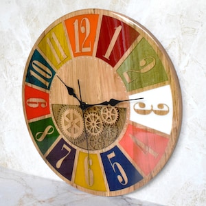 May include: A colorful wooden clock with a gear design in the center. The clock face is divided into 12 sections, each painted a different color. The numbers 1 through 12 are printed on the clock face in a black font.