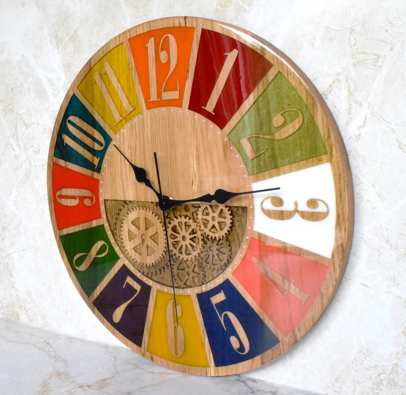 May include: A colorful wooden clock with a gear design in the center. The clock face is divided into 12 sections, each painted a different color. The numbers 1 through 12 are printed on the clock face in a black font.