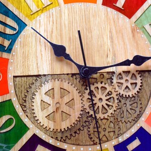 May include: A colorful wooden clock with Roman numeral hour markers and a black metal gear design. The clock face is divided into 12 sections, each painted a different color. The clock hands are black metal.