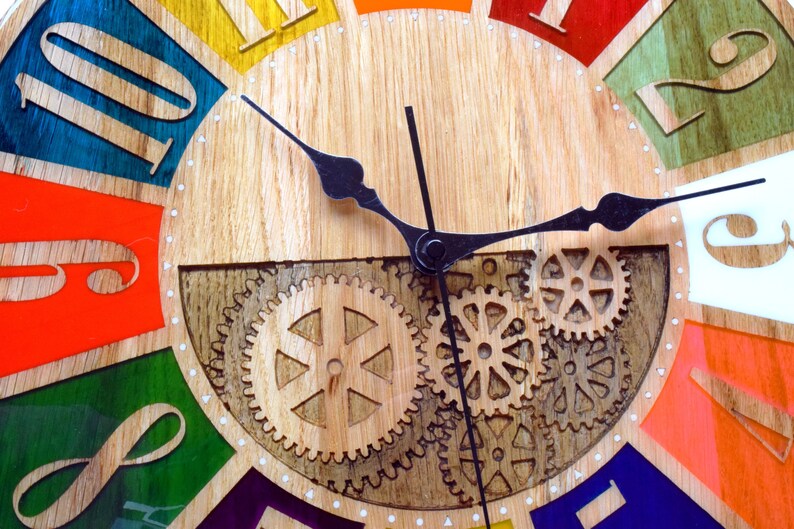 May include: A colorful wooden clock with Roman numeral hour markers and a black metal gear design. The clock face is divided into 12 sections, each painted a different color. The clock hands are black metal.