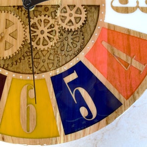 May include: A wooden clock face with colorful segments and a gear design. The numbers 5, 6, 7, and 8 are visible. The clock face is made of wood and has a white background.