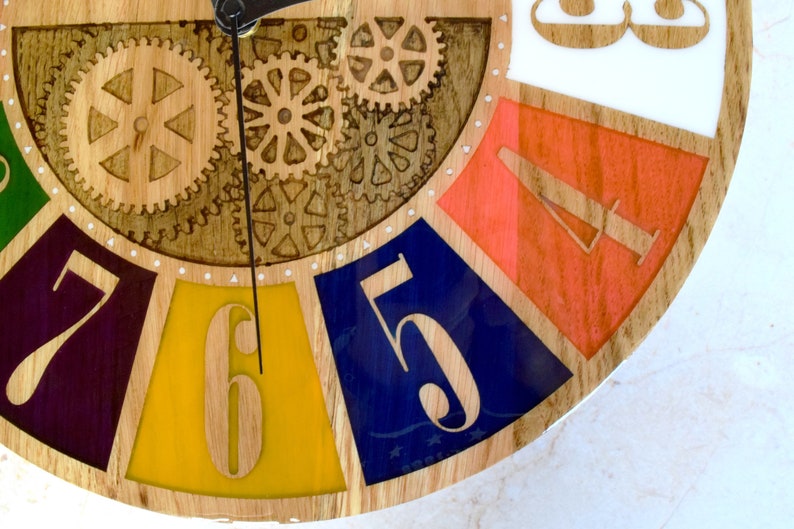 May include: A wooden clock face with colorful segments and a gear design. The numbers 5, 6, 7, and 8 are visible. The clock face is made of wood and has a white background.