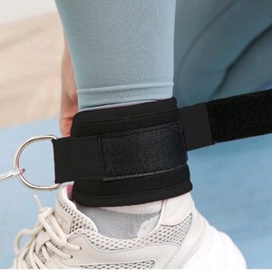 May include: Black ankle weight with an adjustable strap and a metal ring. The weight is worn on a person's ankle over a white sneaker.