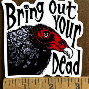 May include: A white sticker with the text "Bring Out Your Dead" in black, gothic-style lettering. The sticker features a detailed illustration of a vulture with a red head and beak, and black and white feathers.