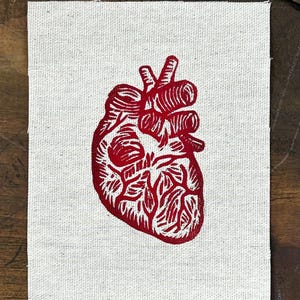 May include: A red anatomical heart illustration printed on a white fabric patch.
