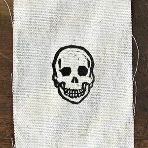 May include: A black and white skull design printed on a white fabric patch.