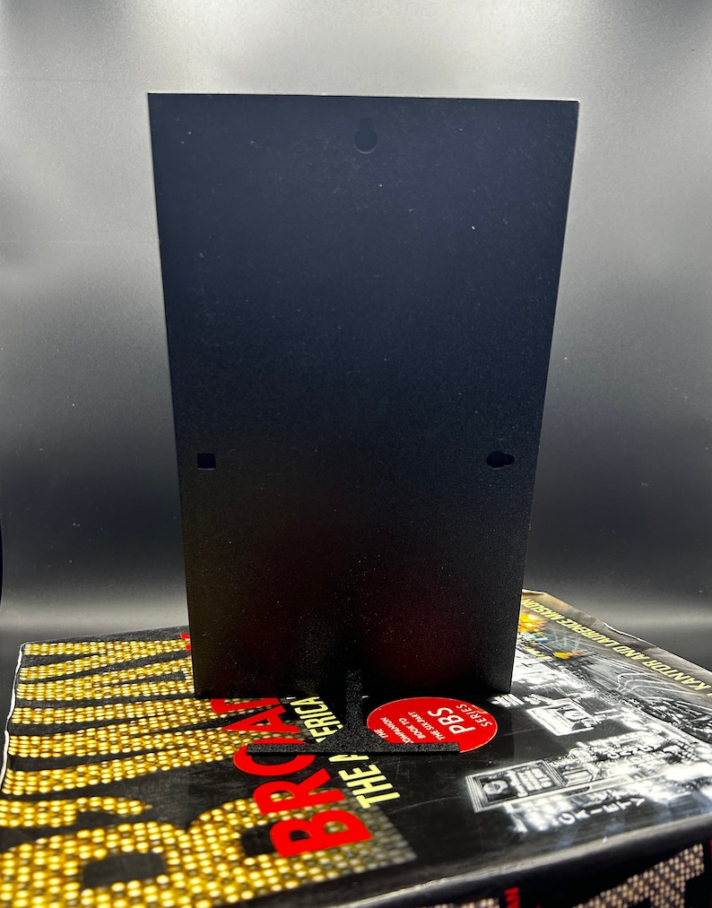 May include: A black metal stand with a hole at the top. The stand is sitting on a book with the title "The America" and the PBS logo.