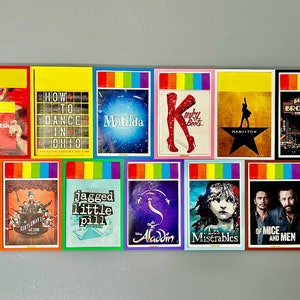 Könnte beinhalten: Eine Wanddekoration mit Broadway-Showplakaten mit Regenbogenrändern. Die Poster zeigen Titel wie "Tootsk", "How to Dance in Ohio", "Matilda", "Kinky Boots", "Hamilton", "Jagged Little Pill", "Aladdin", "Les Misérables", "Of Mice and Men" und "Bullets Over Broadway".