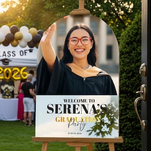 May include: A graduation party welcome sign on an easel. The sign features a photo of a smiling graduate in a cap and gown, with the text "Welcome to Serena's Graduation Party" and the date June 04, 2026.