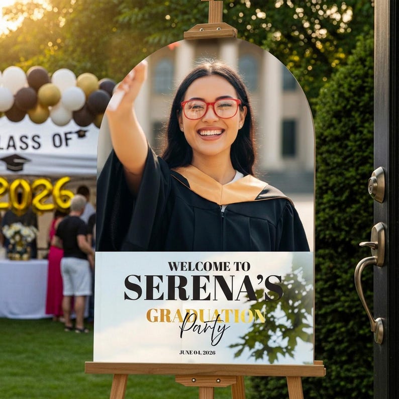 May include: A graduation party welcome sign on an easel. The sign features a photo of a smiling graduate in a cap and gown, with the text "Welcome to Serena's Graduation Party" and the date June 04, 2026.