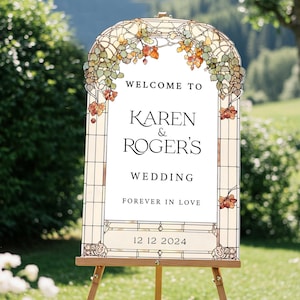 May include: An arched wedding sign featuring a stained glass border with green and orange leaf motifs. The white center displays the text: WELCOME TO KAREN & ROGER'S WEDDING FOREVER IN LOVE 12 12 2024. The sign is mounted on a wooden easel.