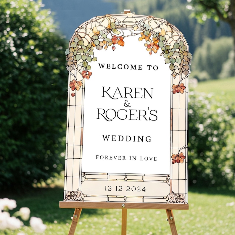May include: An arched wedding sign featuring a stained glass border with green and orange leaf motifs. The white center displays the text: WELCOME TO KAREN & ROGER'S WEDDING FOREVER IN LOVE 12 12 2024. The sign is mounted on a wooden easel.