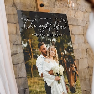 May include: A rectangular vertical sign on an easel featuring a photograph of a couple and a horse in a field. The text reads "WELCOME TO The night before" in white script and "ADELINE & GEORGE" in white capital letters over the photo.