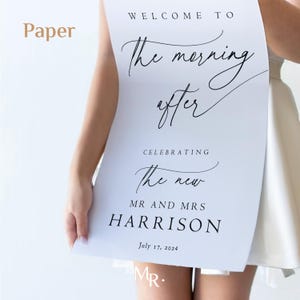 K&ouml;nnte beinhalten: Ein wei&szlig;es Schild mit schwarzer Kalligraphie, auf dem steht "Willkommen zum Morgen danach, wir feiern das neue Ehepaar Harrison, 17. Juli 2024".