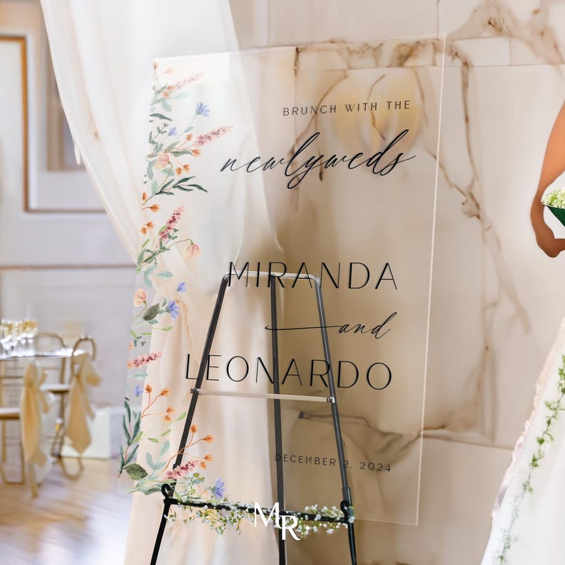K&ouml;nnte beinhalten: Klares Acryl-Hochzeitschild mit Aquarell-Blumenmuster. Das Schild lautet "Brunch mit den Frischverm&auml;hlten Miranda und Leonardo 2. Dezember 2023".
