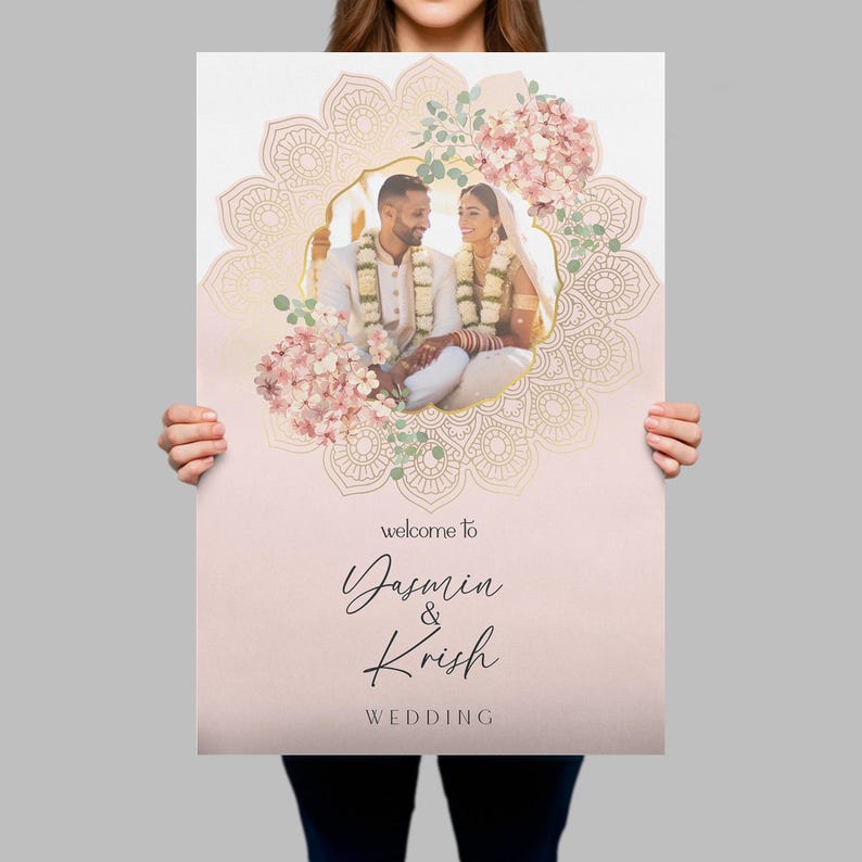 Peut inclure: Un panneau de bienvenue de mariage rectangulaire avec une photo centrale d'un couple en tenue traditionnelle, encadr&eacute;e par un motif mandala dor&eacute; et des fleurs roses. Le texte indique : welcome to Yasmin & Krish WEDDING en noir.