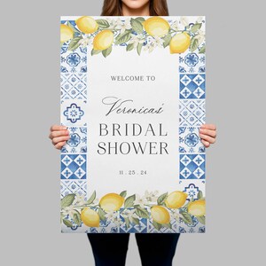 May include: A rectangular sign featuring a white centre with the text WELCOME TO, Veronica's, BRIDAL SHOWER, and 11.25.24. The border consists of blue and white patterned tiles, with yellow lemons and green leaves at the top and bottom edges.