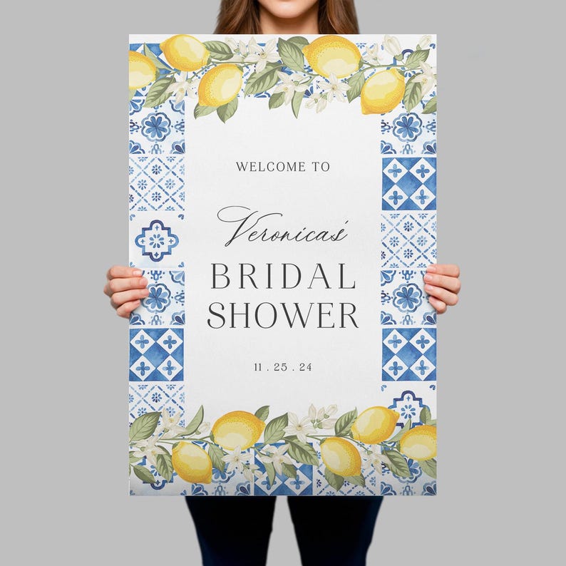May include: A rectangular sign featuring a white centre with the text WELCOME TO, Veronica's, BRIDAL SHOWER, and 11.25.24. The border consists of blue and white patterned tiles, with yellow lemons and green leaves at the top and bottom edges.
