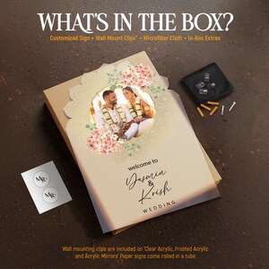 Peut inclure: Une enseigne rectangulaire avec un cadre circulaire central contenant la photographie d'un couple, entour&eacute;e d'illustrations de fleurs roses et de feuilles vertes. Le texte indique "welcome to Yasmin & Krish WEDDING". Inclut des clips de fixation.