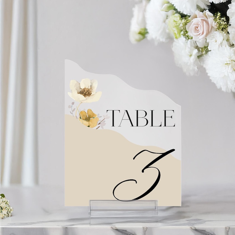 Puede incluir: Una tarjeta de n&uacute;mero de mesa beige con un dise&ntilde;o floral blanco y el texto "TABLE 3" en negro.