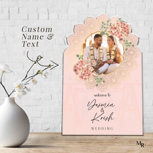 Peut inclure: Un panneau de bienvenue de mariage rectangulaire avec un fond rose p&acirc;le et un cadre dor&eacute; en forme d'arche mandala. Le panneau pr&eacute;sente une photo d'un couple, des accents floraux et le texte : welcome to Yasmin & Krish WEDDING. Custom Name & Text.