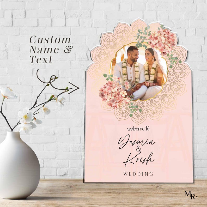 Peut inclure: Un panneau de bienvenue de mariage rectangulaire avec un fond rose p&acirc;le et un cadre dor&eacute; en forme d'arche mandala. Le panneau pr&eacute;sente une photo d'un couple, des accents floraux et le texte : welcome to Yasmin & Krish WEDDING. Custom Name & Text.