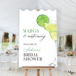 May include: White sign with green and black text that reads "Margs & Matrimony Welcome to Sabrina's Bridal Shower". A green lime wedge and a glass of margarita are illustrated on the sign.