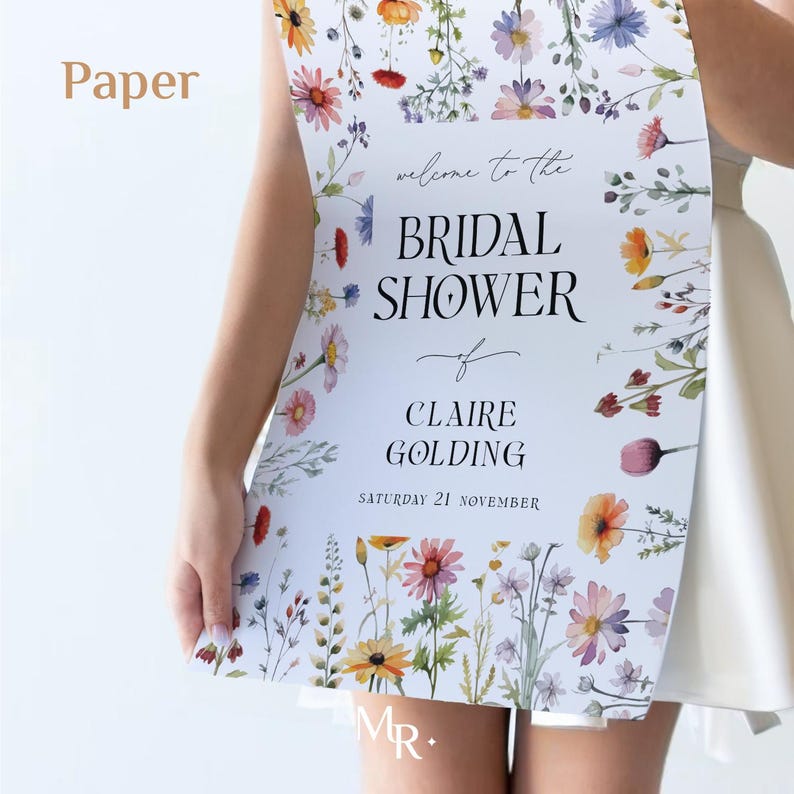 May include: A vertical rectangular sign printed on paper featuring a white background with colorful watercolor wildflowers along the top and bottom edges. The text reads: welcome to the BRIDAL SHOWER of CLAIRE GOLDING SATURDAY 21 NOVEMBER.