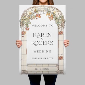 May include: A rectangular wedding sign featuring a stained glass archway design with green and orange foliage. The text reads: WELCOME TO KAREN & ROGER'S WEDDING FOREVER IN LOVE 12 12 2024. The sign has a white background and a grid-like border.