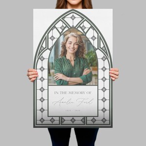 May include: A memorial print featuring a photo of a woman within a gray, arched frame. The text "IN THE MEMORY OF" is above the name "Amelia Ford" and the years "1923 - 2024". The frame has a decorative, stained-glass window design.