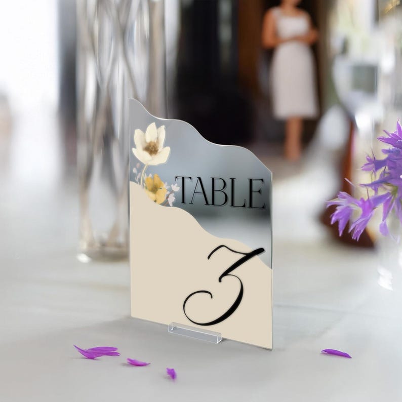 Puede incluir: Una tarjeta de n&uacute;mero de mesa blanca y dorada con un dise&ntilde;o floral y el texto "TABLE 3".