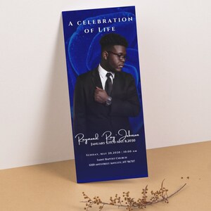 May include: A blue and white funeral program with a photo of a man in a suit. The program includes the text "A Celebration of Life", "Raymond Ray Johnson", "January 3, 1970 - May 8, 2030", "Sunday, May 20, 2030 | 10:00 AM", "Saint Baptist Church", and "1250 Anystreet Anycity, NT 96707".