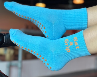 May include: A pair of light blue socks with orange grip dots on the bottom. The socks have the text "Get a Grip" printed on the side in orange.