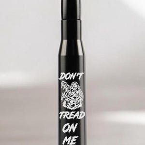 May include: A black bullet-shaped bottle stopper with a pointed tip. The stopper features the words "DON'T TREAD ON ME" in white, along with a graphic of a coiled snake.