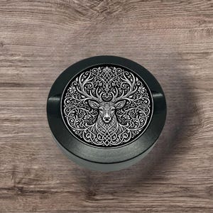 Puede incluir: Un objeto redondo decorativo en blanco y negro con una ilustración detallada de un ciervo con astas ornamentadas y un diseño de nudo celta. El ciervo está centrado, rodeado de patrones arremolinados.