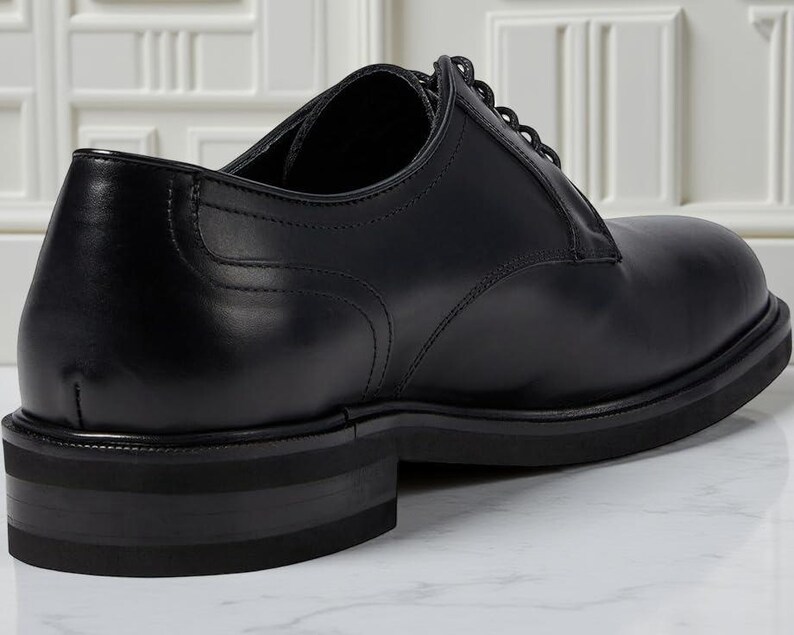 May include: A black leather dress shoe with a rounded toe and a thick sole. The shoe features a lace-up design and a low heel. The shoe is made of smooth, polished leather and is suitable for formal occasions.
