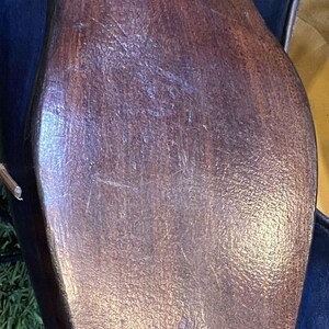May include: Close-up of the sole of a dark blue leather shoe. The sole is made of dark brown wood with visible grain and small metal studs along the edge. The shoe is on a green surface.