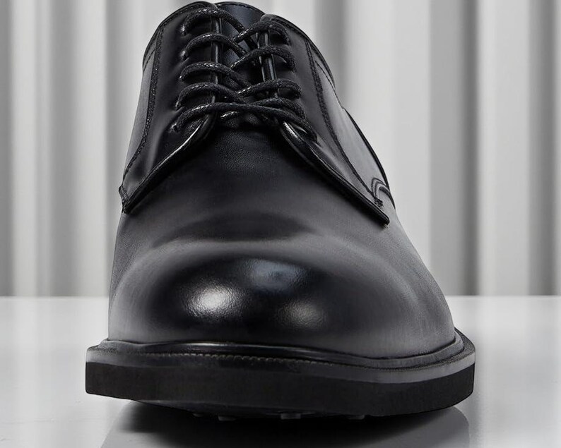 May include: A close-up shot of a black leather dress shoe with laces. The shoe has a glossy finish and a thick sole. The laces are neatly tied, and the shoe appears to be new.