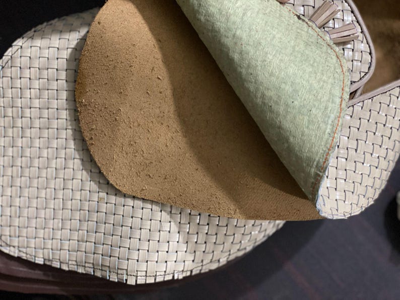 May include: Close-up of a woven leather shoe with a light beige color. The interior reveals a tan suede insole and a light green lining. The shoe's design features a basket weave pattern.