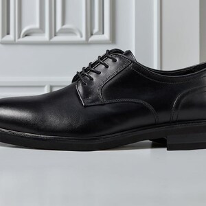 May include: A single black leather dress shoe with a rounded toe and a low heel. The shoe has a lace-up closure and a smooth, polished finish. The shoe is designed for formal occasions.