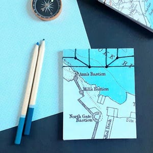 May include: A light blue map print with the text "St Ann's Bastion" and "North Gate Bastion". Two pencils with blue tips and a compass are also visible. The items are on a light blue patterned paper.