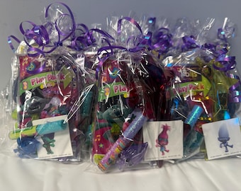 May include: Several gift bags wrapped in clear cellophane and tied with purple ribbon. Each bag contains a "Play Pack" with Trolls characters, glittery tubes, and stickers. The bags are arranged on a white surface.