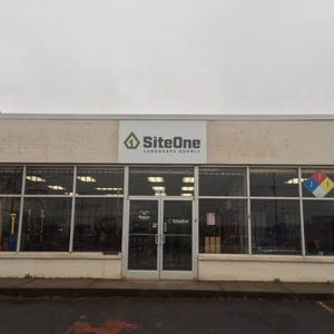 Op de afbeelding: Buitenaanzicht van een SiteOne Landscape Supply winkel. Het gebouw heeft grote glazen ramen en een dubbele deuringang. De naam en het logo van de winkel staan boven de ingang. Het gebouw is lichtbeige geschilderd.